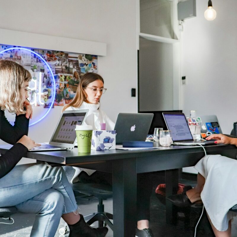 3 women sitting on chair in front of table with laptop computers
